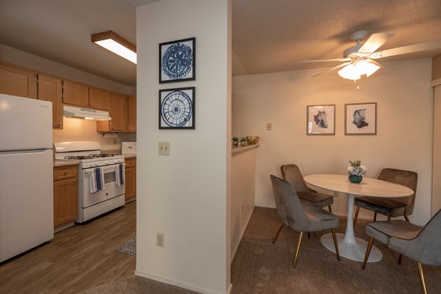 Kitchen with wooden cabinets and white appliances next to a dining nook with a round table and chairs.