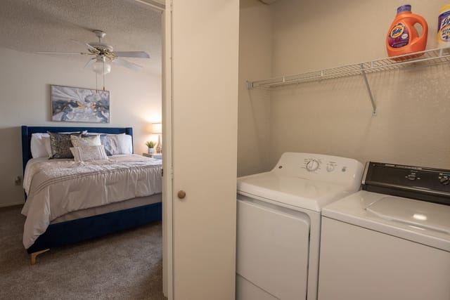 Bedroom with a blue upholstered bed, nightstand, and a laundry closet with a washer and dryer.