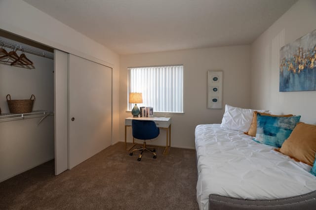 Bedroom with bed, desk, blue chair, open closet, and window with blinds.