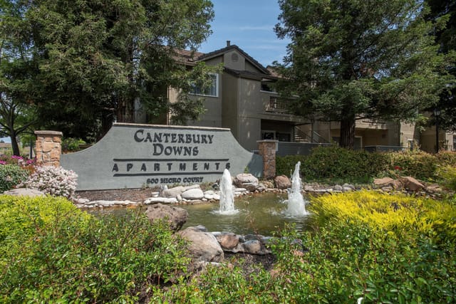 Canterbury Downs Apartments entrance with a water feature and lush landscaping.