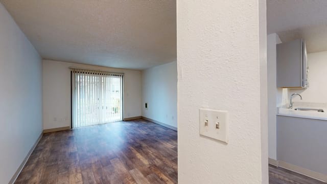 Living room with sliding glass door to patio; kitchen area visible on the right with laminate flooring.