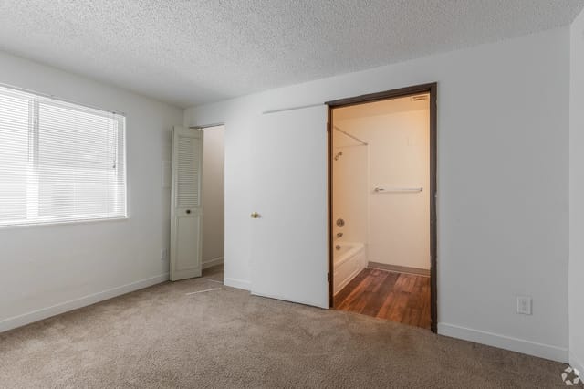 Bedroom with window blinds, beige carpet, and a doorway to an adjacent bathroom.