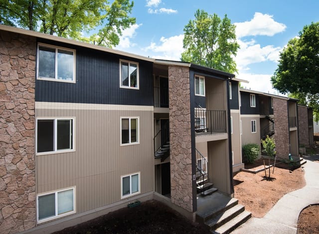 Exterior view of a multi-story apartment building with stone accents, dark siding, and beige siding.