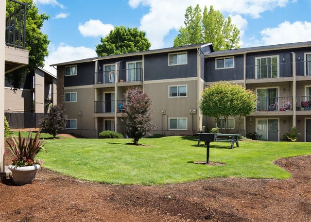Apartment building exterior with balconies, grass, trees, and a picnic area.
