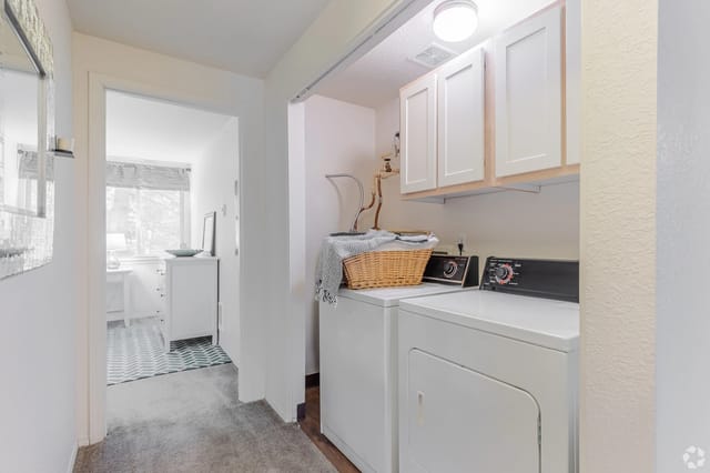 Laundry closet with a washer and dryer, white cabinets above, and a basket on top.