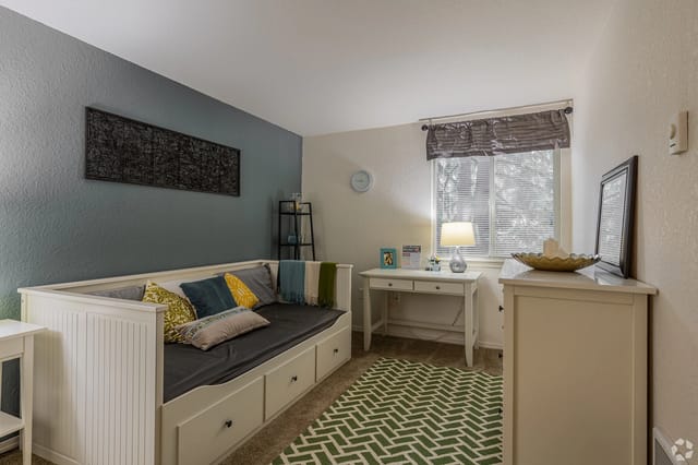 White daybed with storage drawers and colorful pillows against a blue accent wall in a compact living space, with a window nearby.