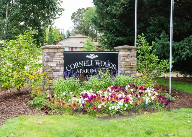 Monument sign reading Cornell Woods Apartments with colorful flower bed and landscaping.