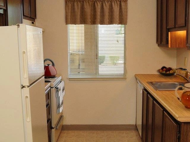 Kitchen with white refrigerator, oven, sink, and wooden countertops.