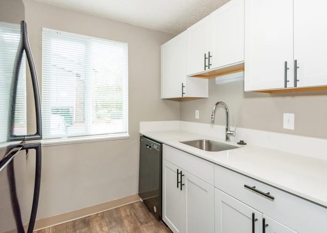 Kitchen with stainless steel refrigerator, white cabinets, quartz countertops, and stainless steel sink.