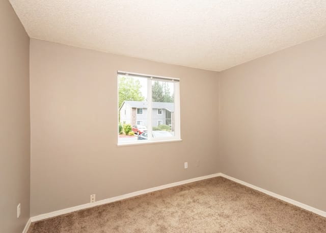 Empty room with neutral walls and carpet, and a large window overlooking the property exterior.