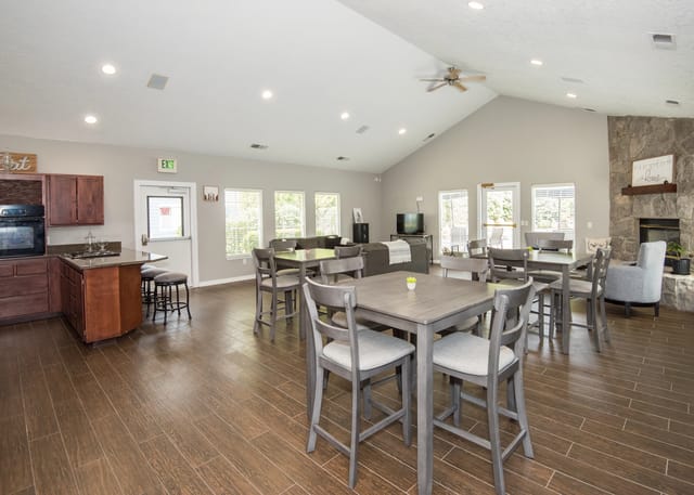Community lounge area with a kitchen, dining tables, seating, and a stone fireplace.