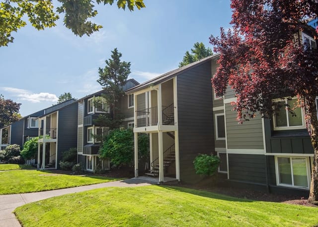 Exterior view of apartment buildings with manicured lawns and trees.
