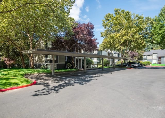 Covered parking area with assigned spots and apartment buildings in the background.