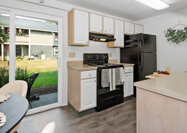Kitchen with black stove, refrigerator, and white cabinets overlooking a backyard.