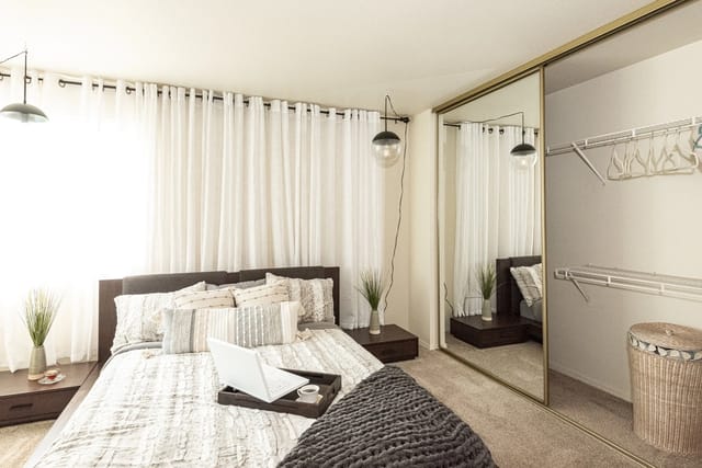 Bedroom with a large bed, white curtains, and mirrored closet doors.