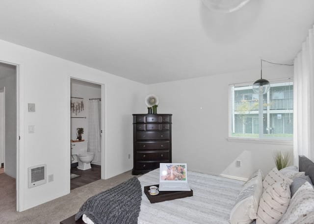 Bedroom with a laptop on the bed and a dresser, with a view of the bathroom.