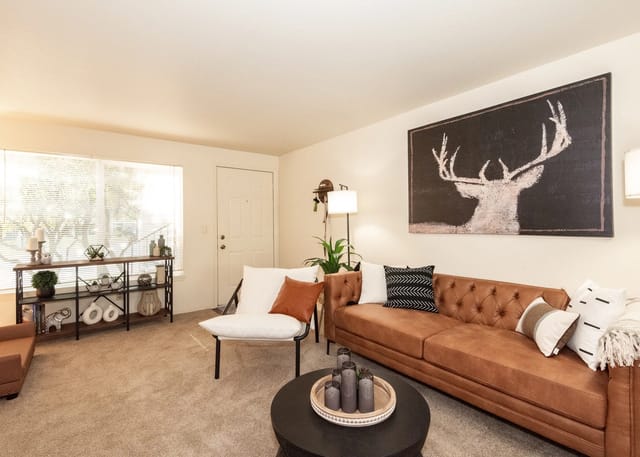Living room with a brown tufted sofa, white accent chair, black coffee table, and a large deer art.