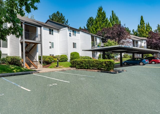 Exterior of apartment buildings with covered parking and green spaces.