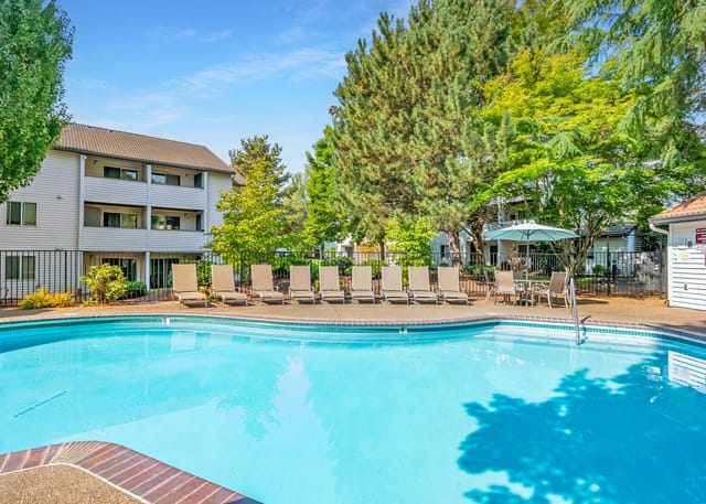 Resort-style swimming pool with lounge chairs and umbrellas, adjacent to apartment buildings.