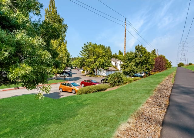 Apartment complex with manicured lawns, trees, and parking lot.