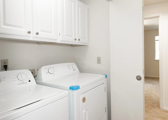 Washer and dryer in a laundry closet with cabinets above.