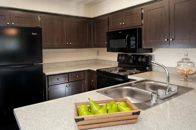 Modern kitchen with dark wood cabinets, black appliances, and granite countertops.