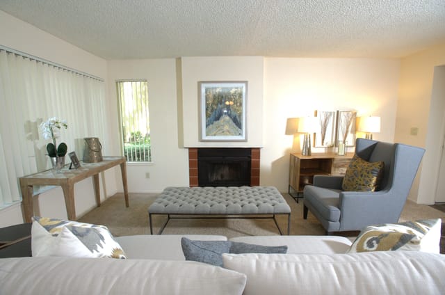 Living room with a fireplace, gray armchair, and tufted ottoman.