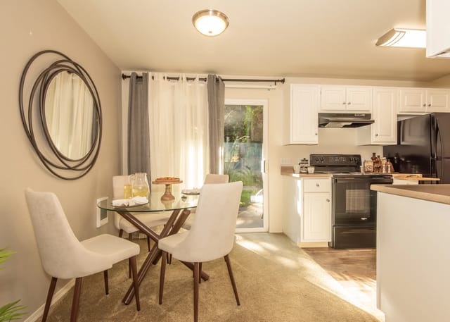 Dining area and kitchen with white cabinets, black appliances, and a glass-top dining table.