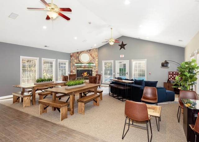 Communal lounge area with large wooden tables, a stone fireplace, and comfortable seating.
