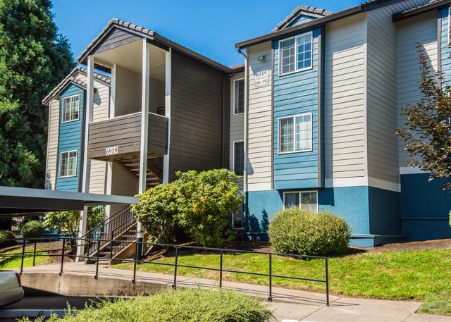 Exterior view of apartment building with covered parking and lush landscaping.