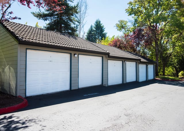 Row of garages with white doors and green trim, surrounded by trees.
