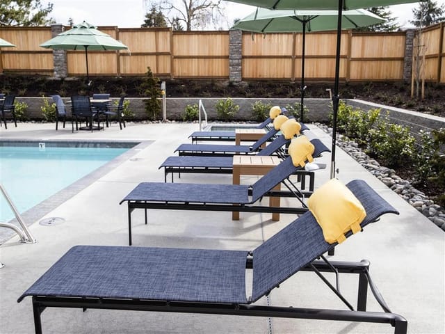 Row of lounge chairs with yellow pillows next to an outdoor swimming pool.