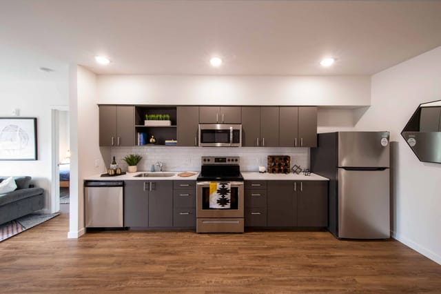 Modern apartment kitchen with dark grey cabinets, stainless steel appliances, and white subway tile backsplash.