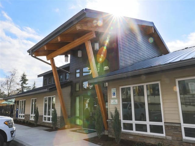 Modern apartment building exterior with wood and metal accents, large windows, and landscaping.