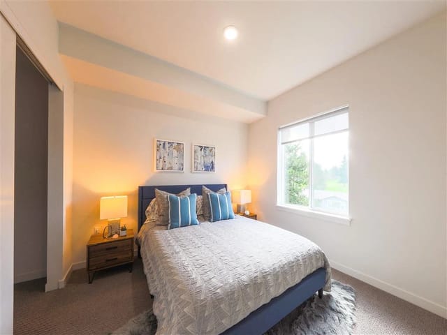 Bedroom with a queen-size bed, blue headboard, bedside tables, and a large window.