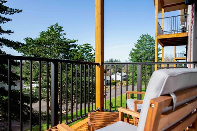 Balcony with seating overlooking a tree-lined street and houses.