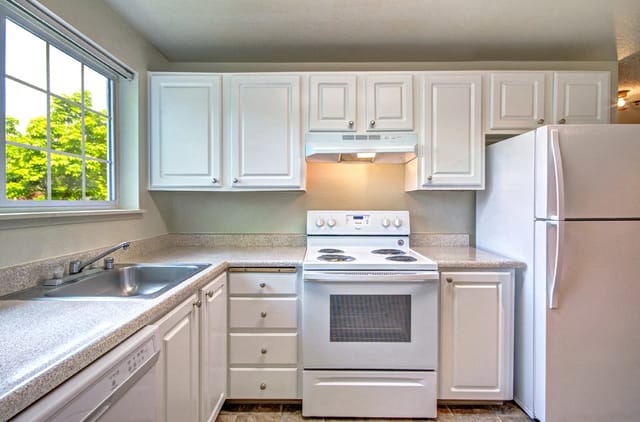 Kitchen with white cabinets, granite countertops, white appliances including a stove and refrigerator, and a sink.