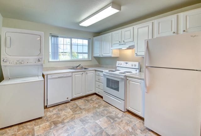 Kitchen with white appliances including a stacked washer and dryer, dishwasher, stove, and refrigerator.