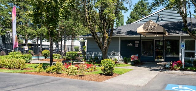 Leasing office entrance with landscaping and outdoor pool visible in background.