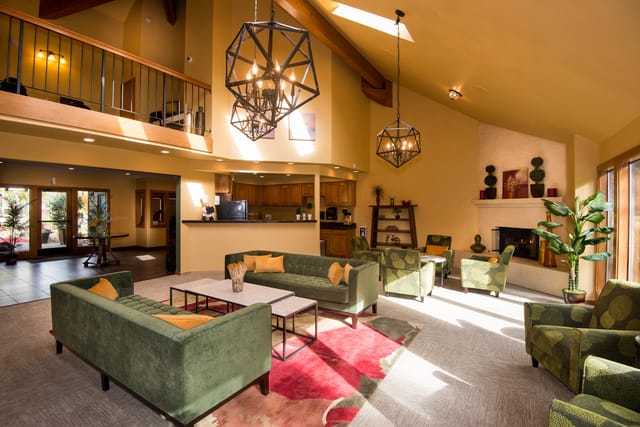 Spacious and bright community lounge with green sofas, modern chandeliers, and a fireplace.