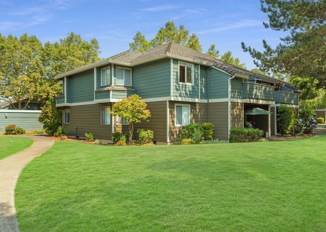 Exterior view of a multifamily apartment building with a green lawn and trees.
