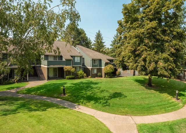 Apartment building exterior with green lawn and trees.