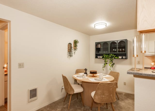 Round dining table with four chairs, a cake, and place settings, next to a decorative cabinet.