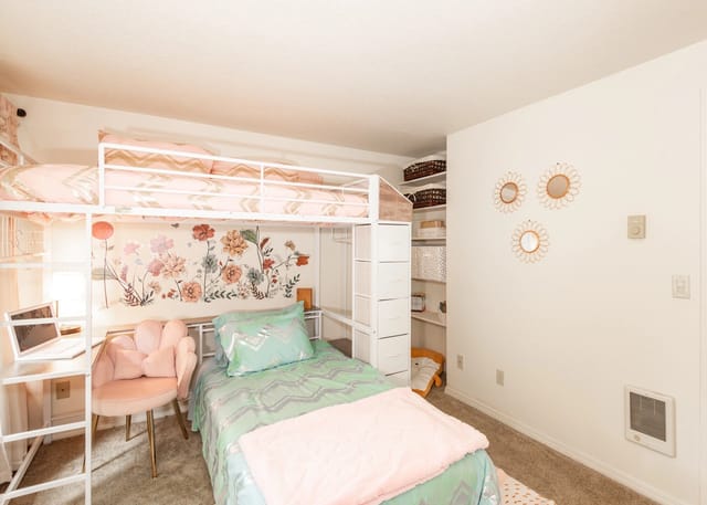 Loft bed with a desk and chair in a bedroom, decorated with floral wall art.