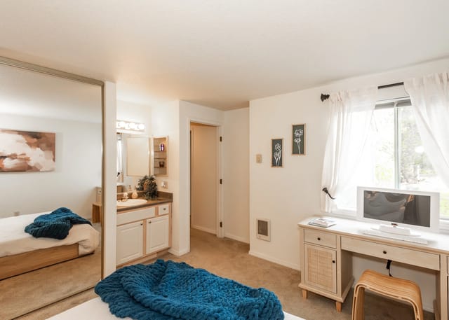 Bedroom with a vanity, mirrored closet, and desk.