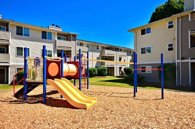 Playground with slides and climbing structures in front of apartment buildings.
