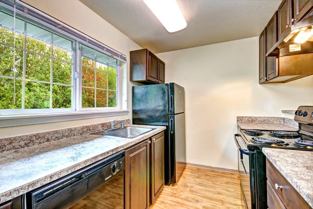 Kitchen with dark wood cabinets, granite countertops, black appliances, and a large window.