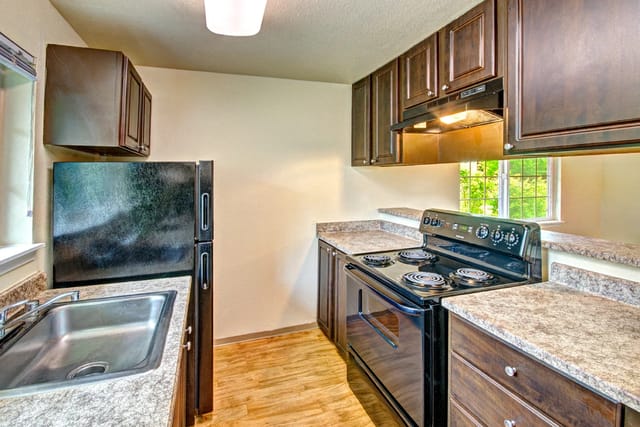 Kitchen with dark wood cabinets, black appliances including a refrigerator and stove, and granite countertops.