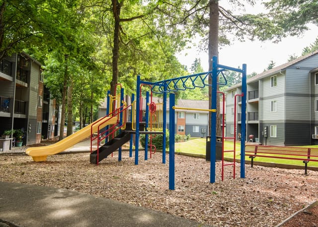 Playground equipment with slide and monkey bars next to apartment buildings.
