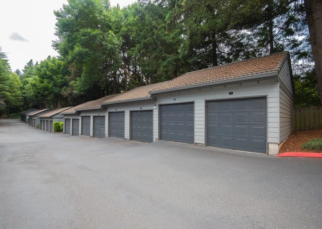 Row of garages with grey doors and numbered bays, surrounded by trees.